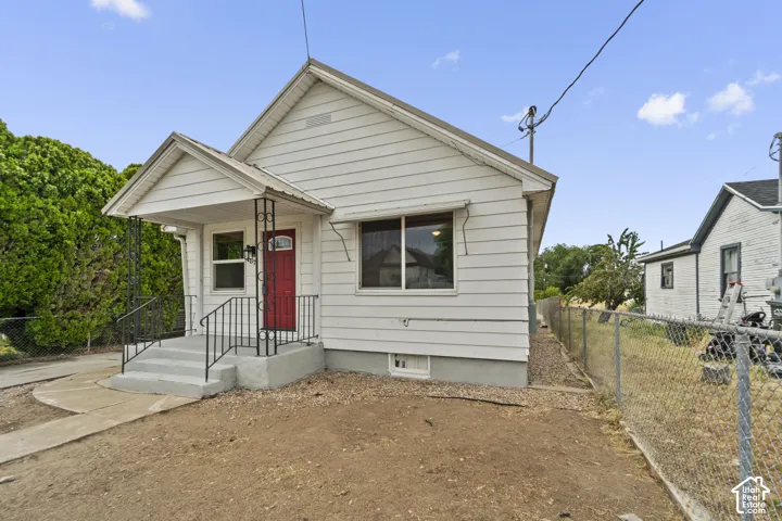 White siding exterior with a red entry door, covered porch, and concrete steps with black railings