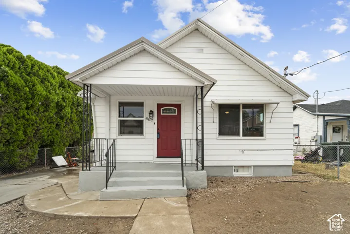 White siding exterior with a red entry door, covered porch, and black wrought iron railings