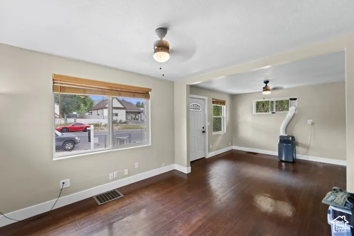 Dark wood-finish flooring with light-toned walls, ceiling fans, and natural light from multiple windows
