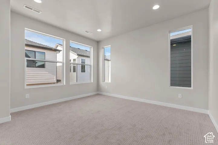 Neutral-toned carpeting and walls, multiple windows providing natural light, and recessed ceiling lighting