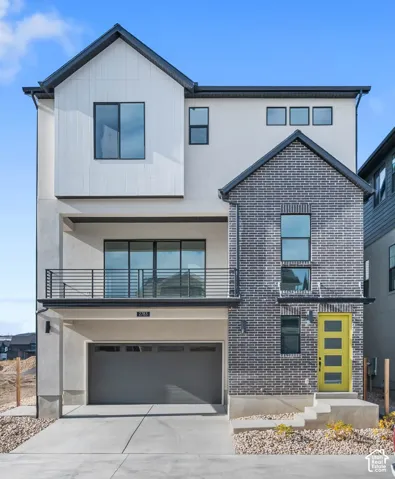 Contemporary exterior featuring mixed material cladding, an attached two-car garage, a second-story balcony with metal railings, a vibrant yellow entry door, and multi-paned windows