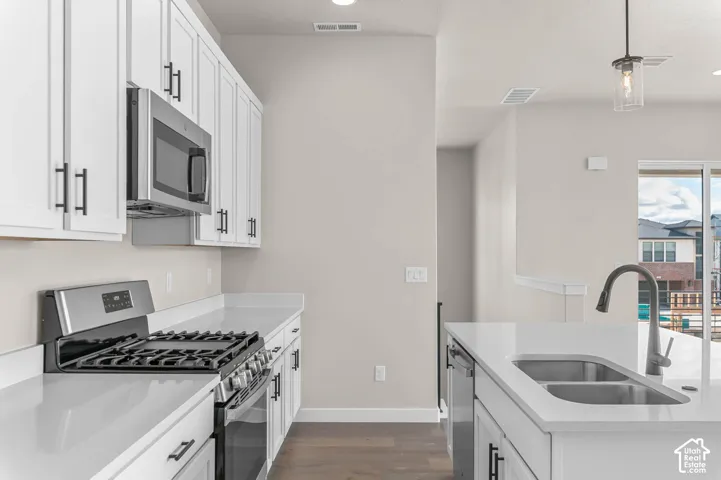 Modern kitchen featuring white shaker cabinetry, stainless steel appliances, light countertops, wood-finish flooring, and a double basin sink with a gooseneck faucet