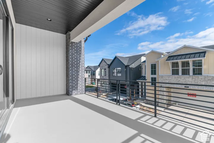 Balcony with a dark gray brick pillar, black metal railing, and white vertical siding