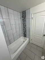 Bathtub with a tiled surround, decorative tile accent, and tiled flooring