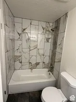 Bathtub with a shower fixture, decorative wall tiling, and wood-finish flooring