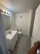 White vanity with an integrated sink and chrome faucet, gray tile flooring, toilet, and modern light fixture