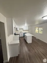 Open concept kitchen featuring an island, white cabinetry, integrated sink, and wood-finish flooring