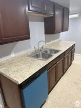 Dark wood-finish cabinetry, light-toned countertops, stainless steel double basin sink with a chrome faucet, and integrated dishwasher