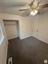 Carpeted flooring, ceiling fan with integrated lighting, built-in closet with shelving and hanging rod, paneled interior door, and window