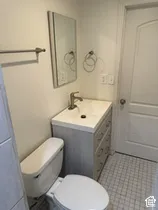 White porcelain toilet, vanity with storage drawers, chrome-finish faucet, wall-mounted mirror, and tiled flooring