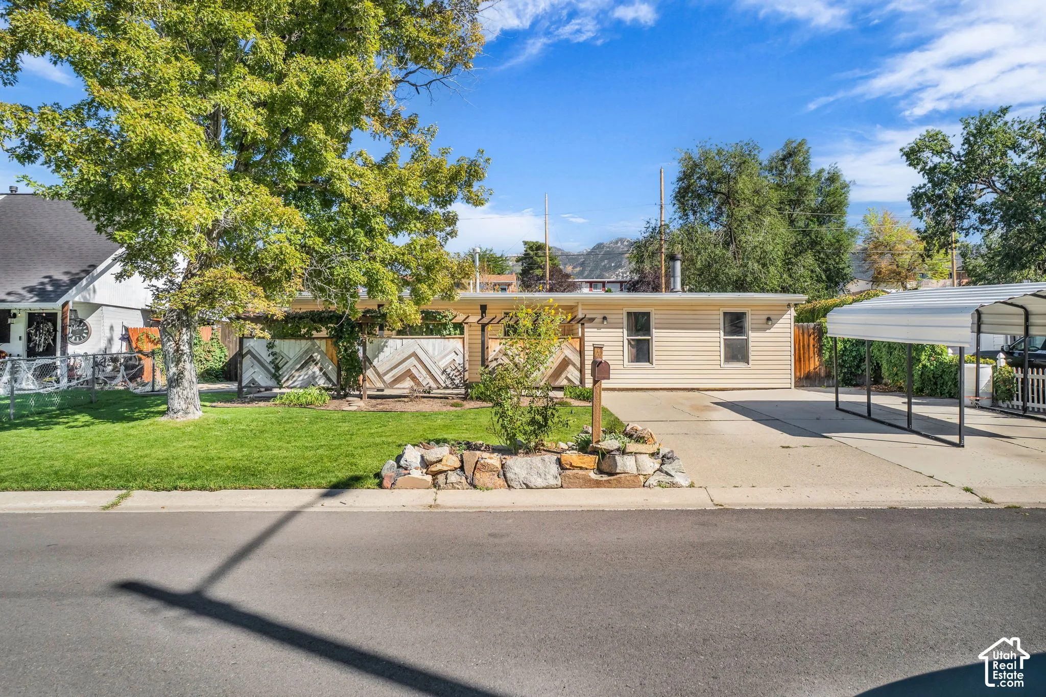 Siding exterior with a covered carport, rock landscaping, and a manicured lawn