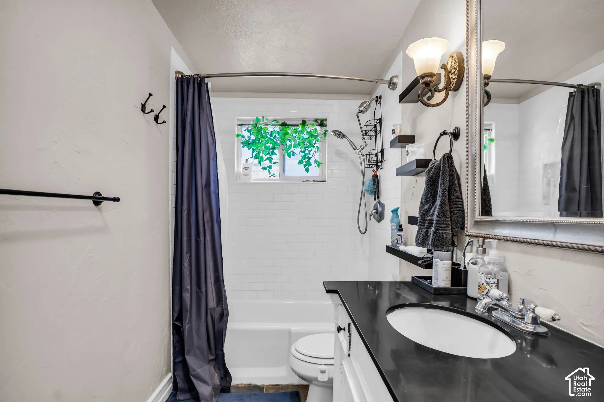 White subway tile shower surround with a window, white bathtub, black countertop vanity with an undermount sink, and a framed mirror