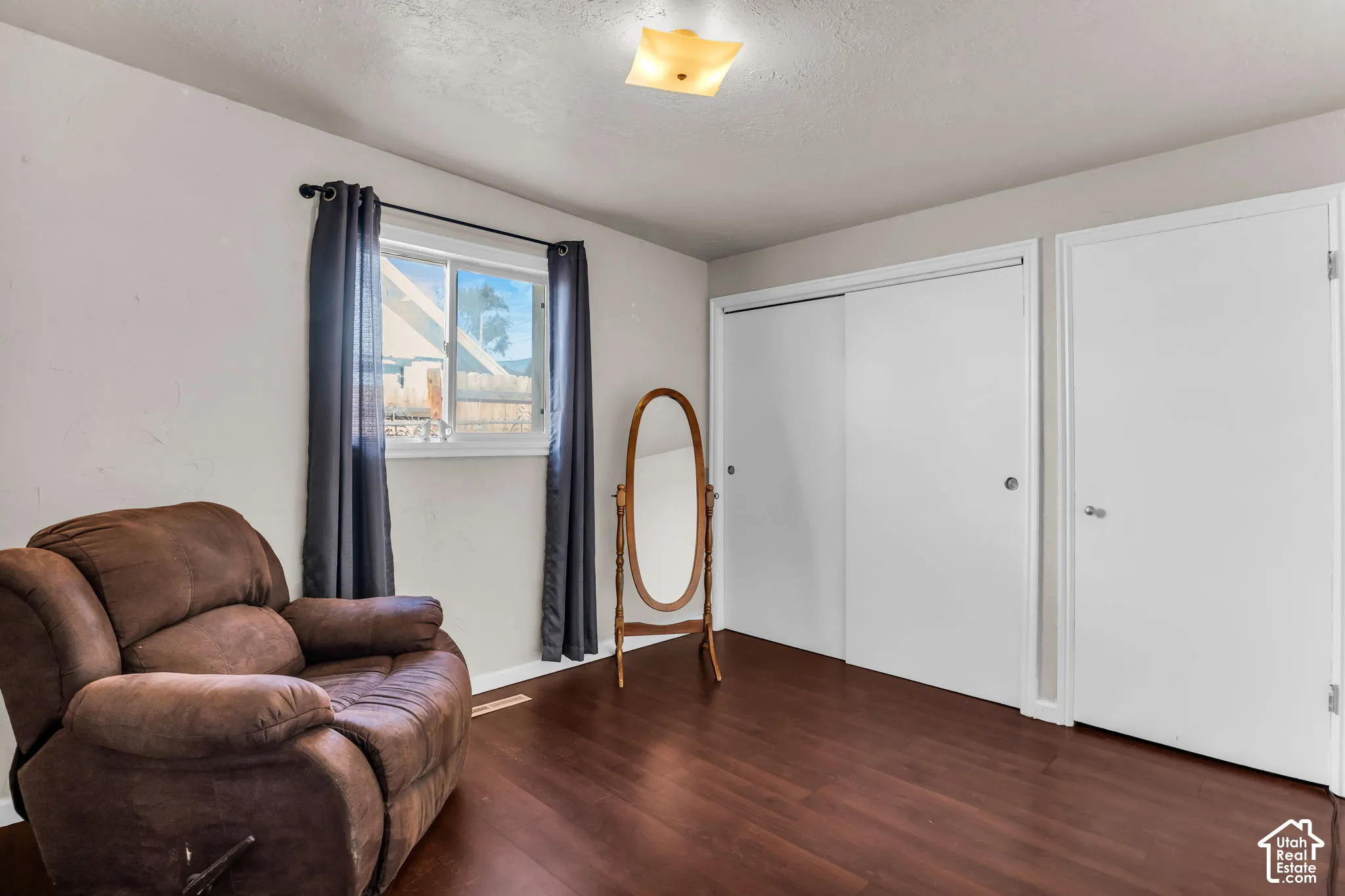 Spacious bedroom showcasing rich wood-finish flooring, a large window with natural light, and dual closets with sliding doors