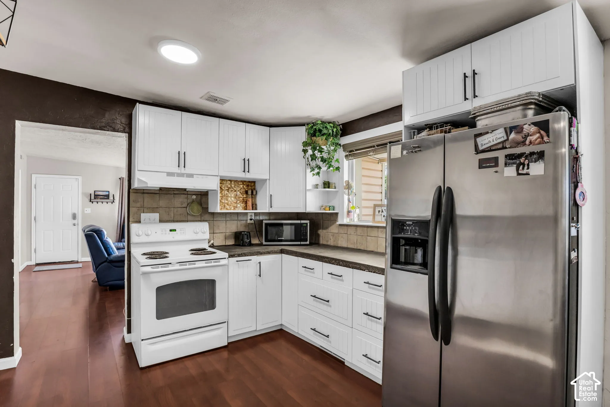 Kitchen featuring white upper and lower cabinetry, stainless steel refrigerator, white electric range, and a tiled backsplash