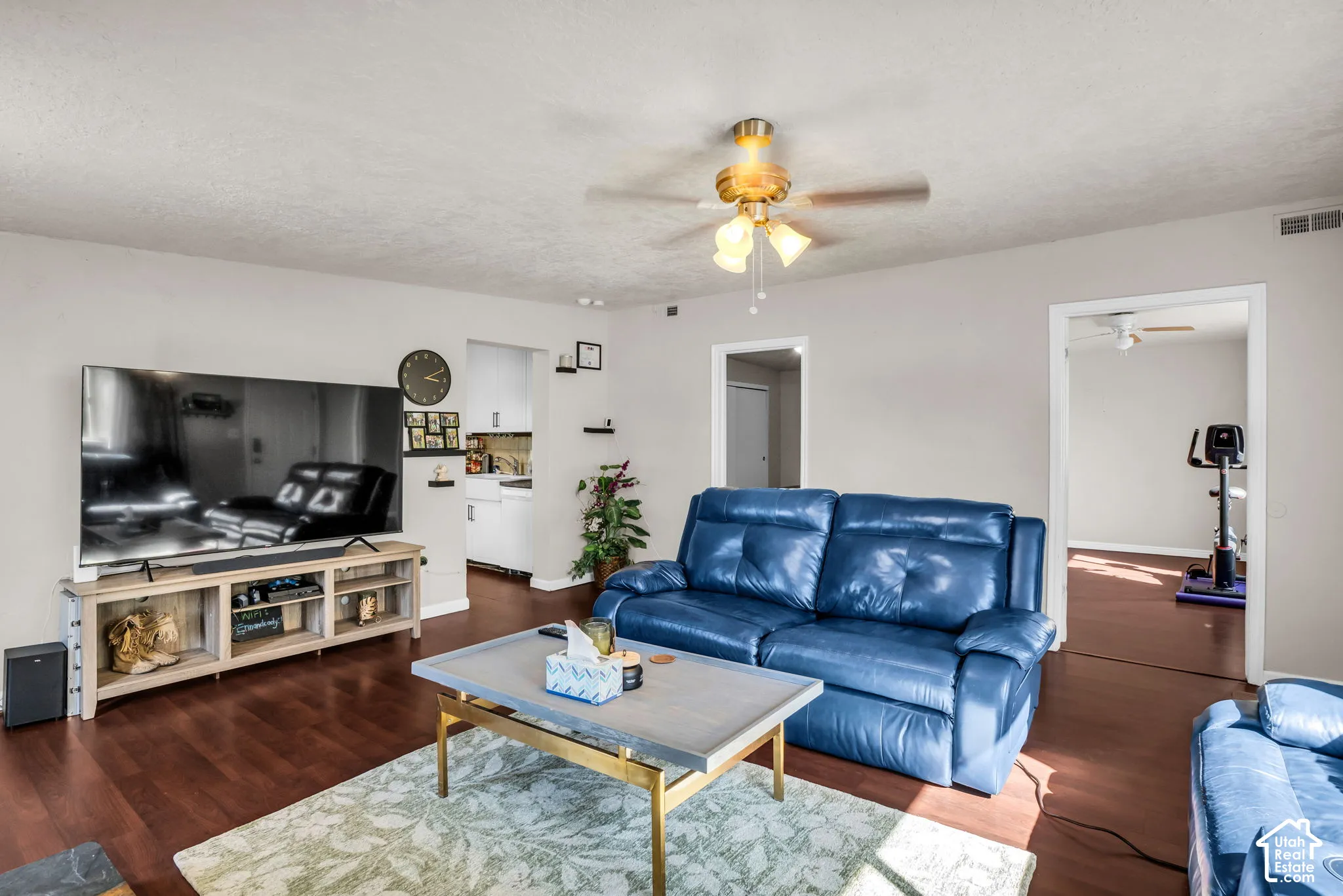 Warm-toned wood-finish flooring, light neutral wall color, and a ceiling fan with integrated lighting