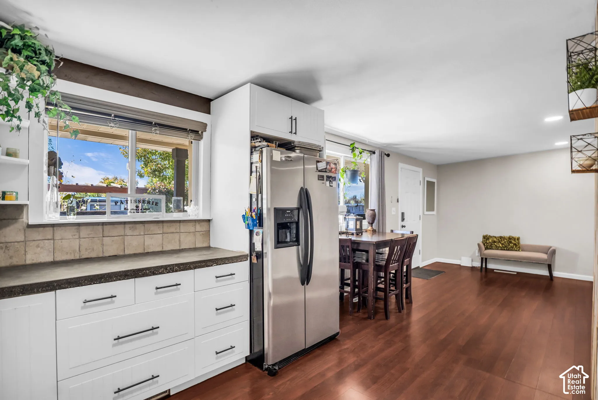 White cabinetry with dark hardware, stainless steel refrigerator, tile backsplash, wood-finish flooring, and recessed lighting