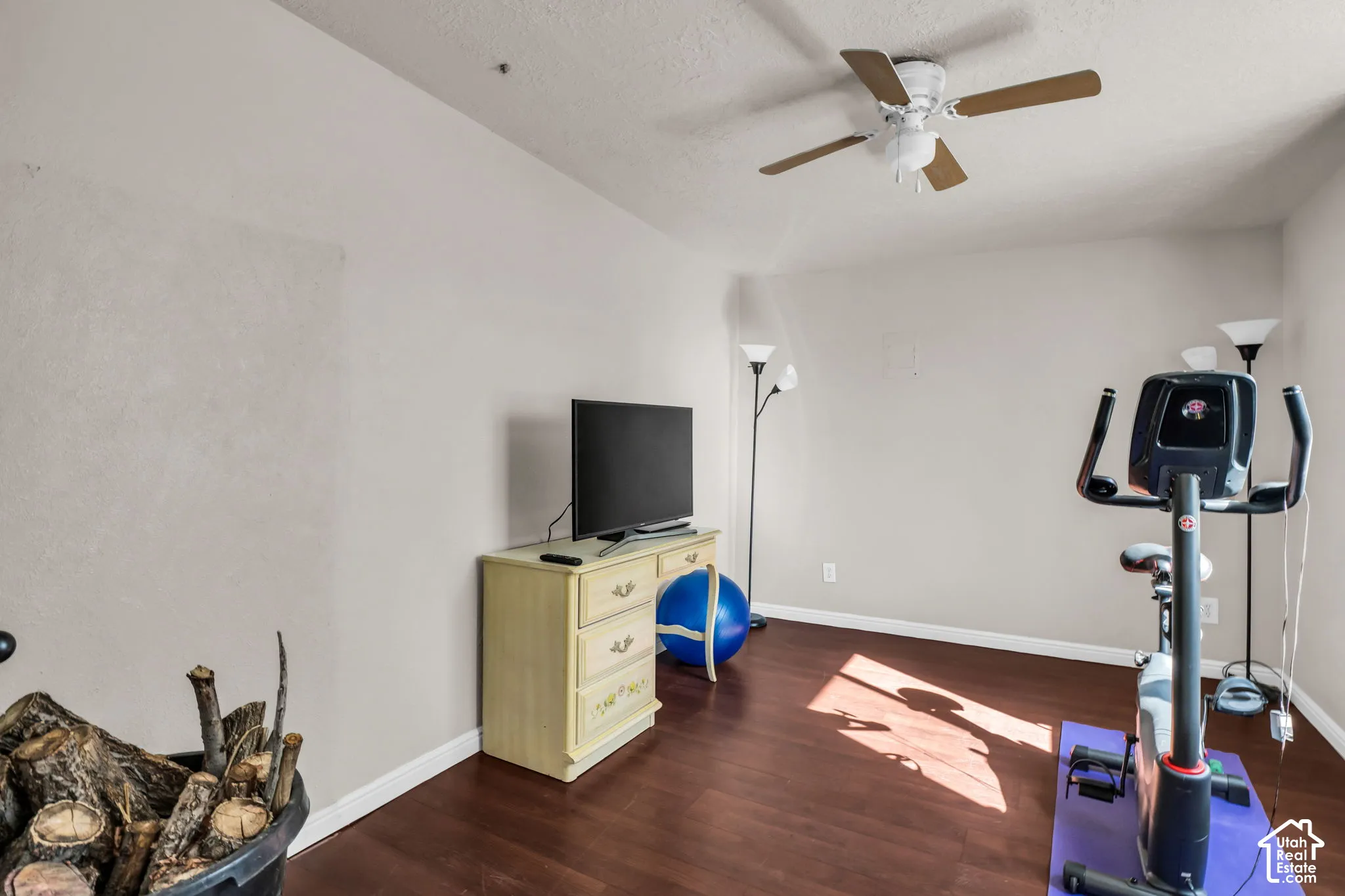 Spacious recreation room featuring hardwood flooring, ceiling fan with integrated lighting, and ample natural light from windows