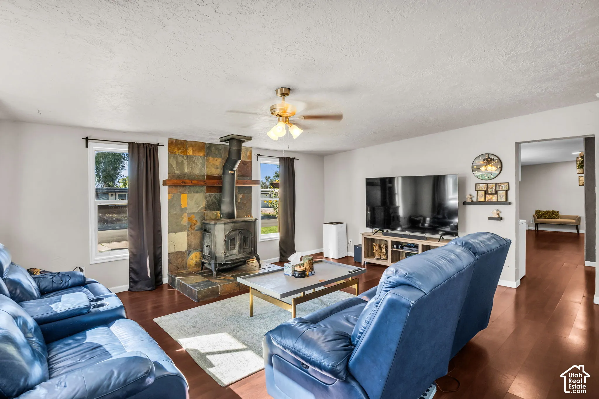 Living area with a built-in wood-burning stove and stone surround, wood-finish flooring, and a ceiling fan