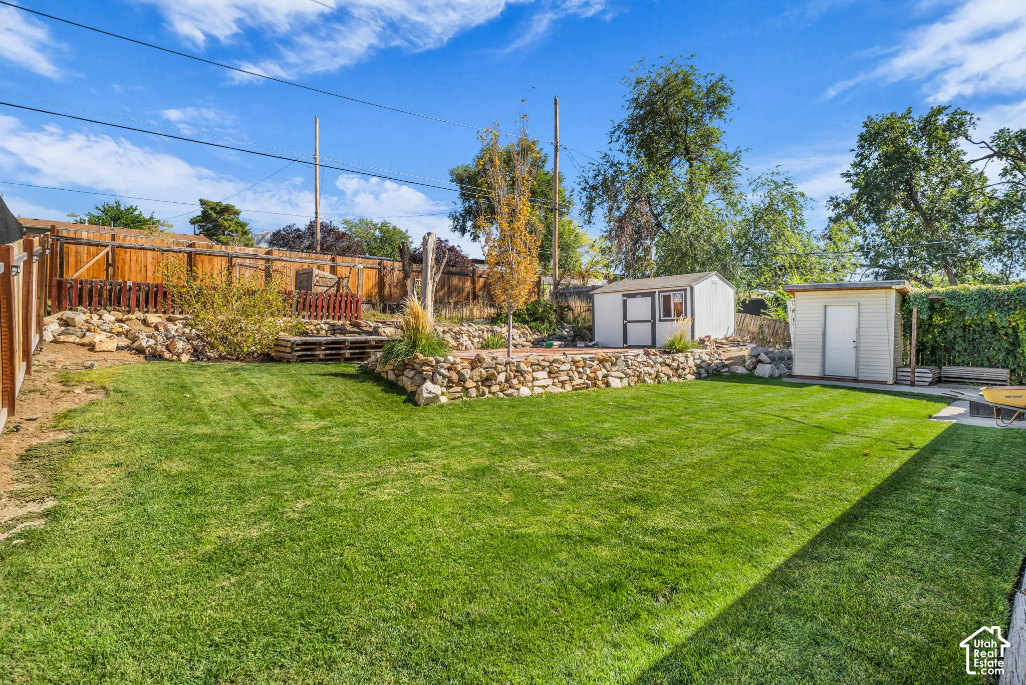 Expansive lawn area with a wood privacy fence, two storage sheds, and a rock-lined terraced garden