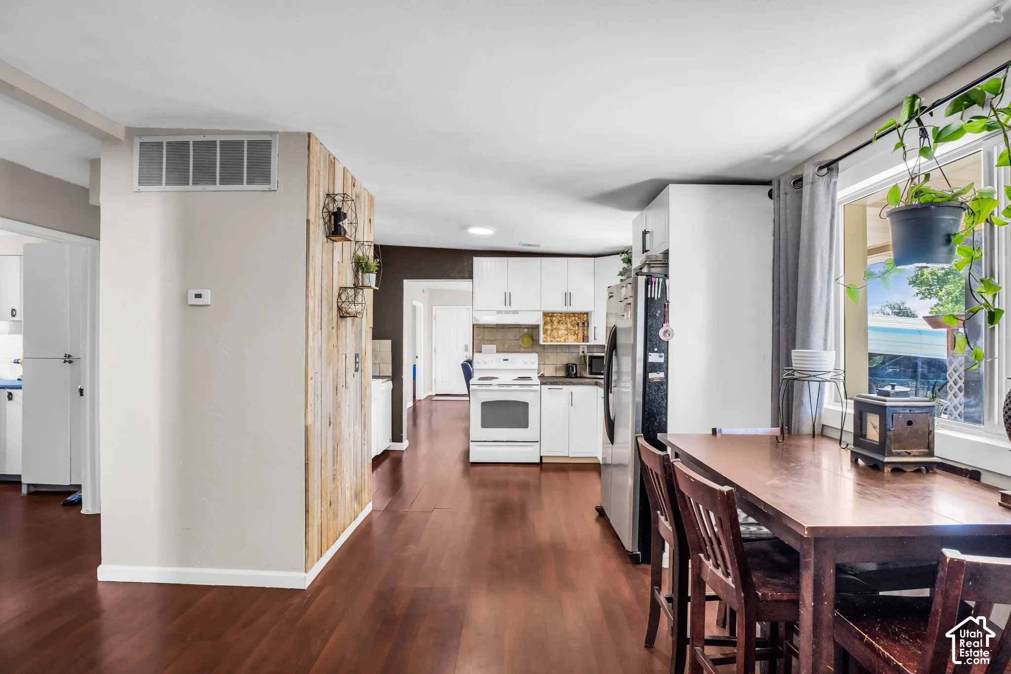 Wood-finish flooring throughout, bright white kitchen cabinetry, stainless steel refrigerator, white range, and a large window with natural light