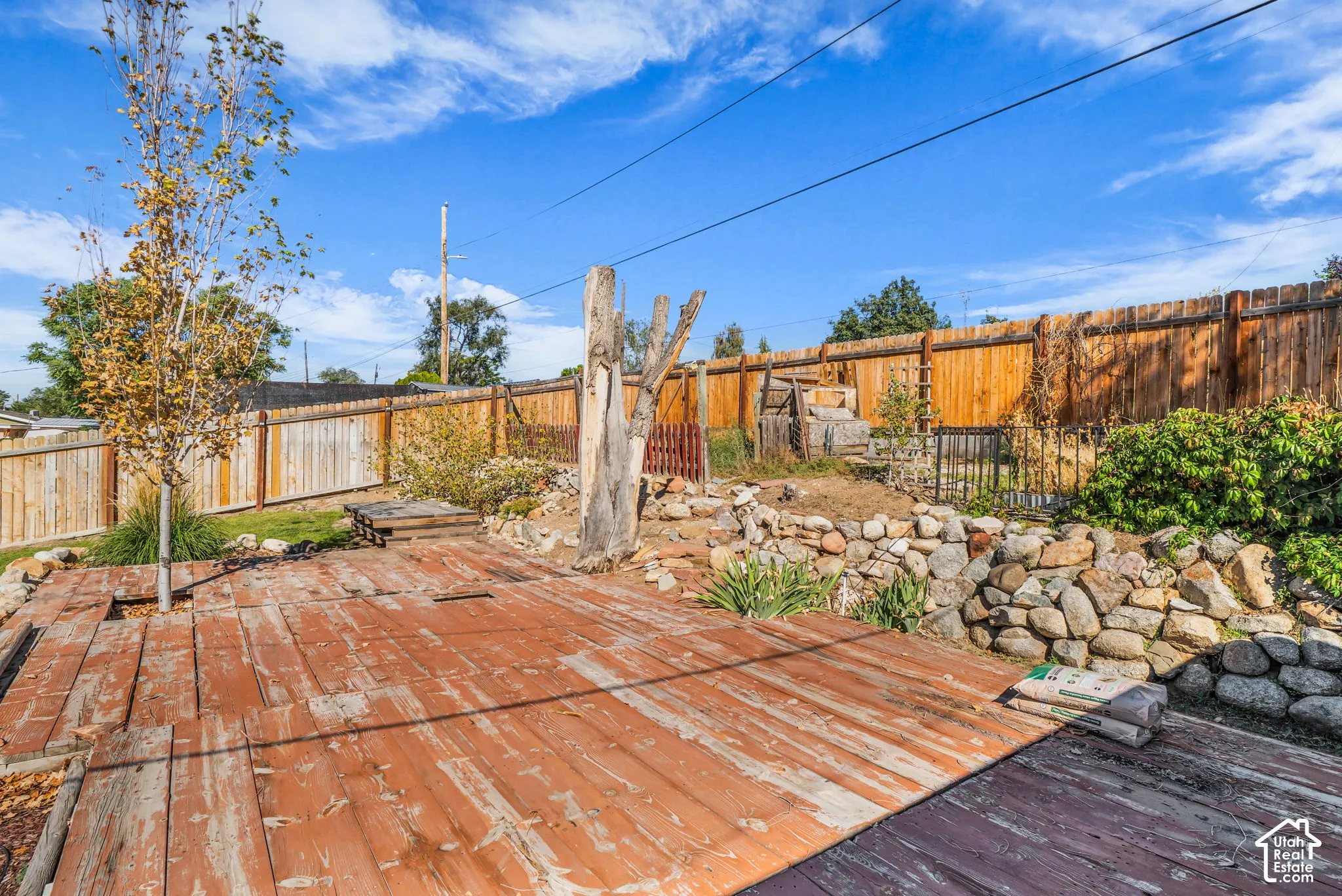 Expansive backyard featuring a wood-plank deck, natural wood fencing, and diverse landscaping with rock elements and mature trees