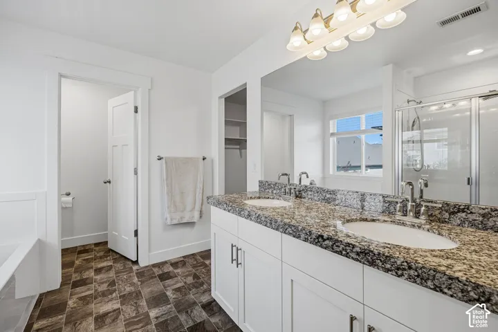 Dual vanity with a patterned countertop and undermount sinks, alongside a glass-enclosed shower, a built-in tub, and a window