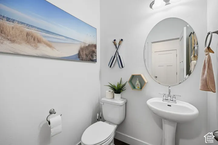 Pedestal sink with chrome faucet, oval mirror, wall-mounted light fixture, and white toilet
