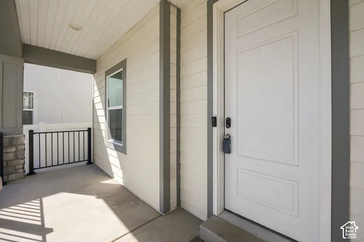 Covered porch with concrete flooring and a black metal railing, featuring a stone-clad column and a panel-style entry door