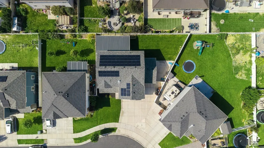 Residential property featuring a shingled roof, solar panel installations, a concrete driveway, and expansive grass lawns in the front and rear