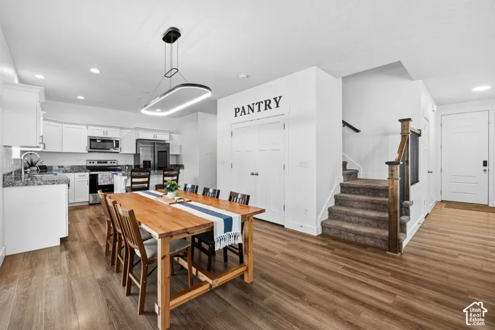 Kitchen and dining area featuring wood-finish flooring, white cabinetry, stainless steel appliances, and a modern linear pendant light fixture