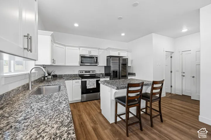 Modern kitchen featuring white cabinetry, stainless steel appliances, granite countertops, wood-finish flooring, and a central island with seating