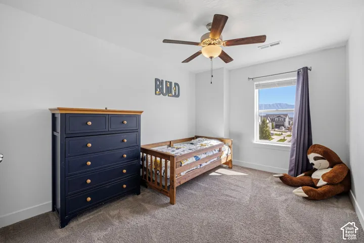 Carpeted room featuring a ceiling fan with light fixture and a window with mountain scenery