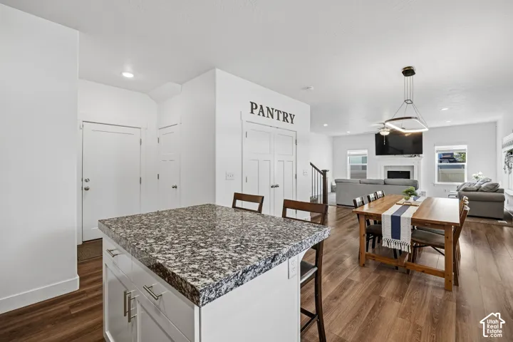 Kitchen island with a granite-style countertop, wood-finish flooring, a dining area with a modern chandelier, and a living area with a built-in fireplace
