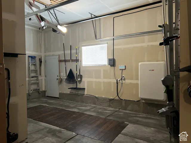 Garage featuring an interior access door, a built-in battery storage system, and a window with blinds