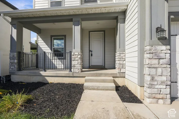 Covered front porch featuring stone-clad columns, black metal railing, and a white panel door