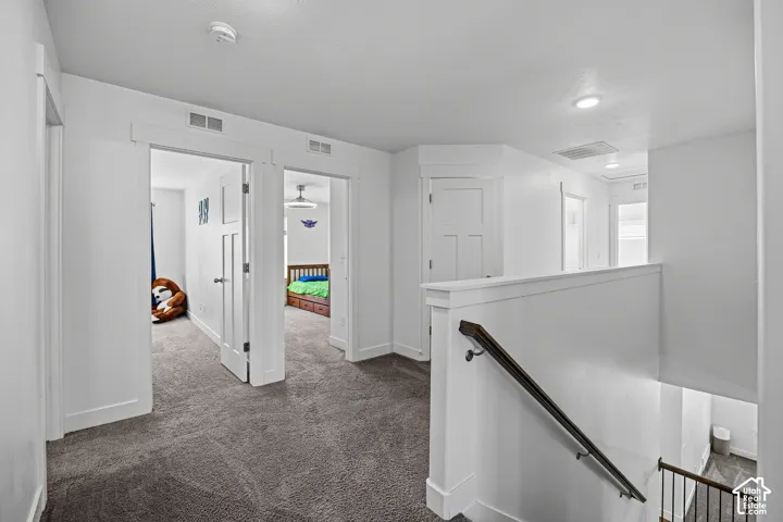 Carpeted hallway with white walls, recessed lighting, and white trim