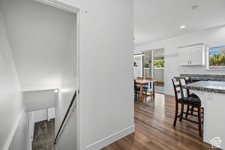 Open-concept living area featuring wood-finish flooring, white cabinetry, granite countertops, and a sliding glass door