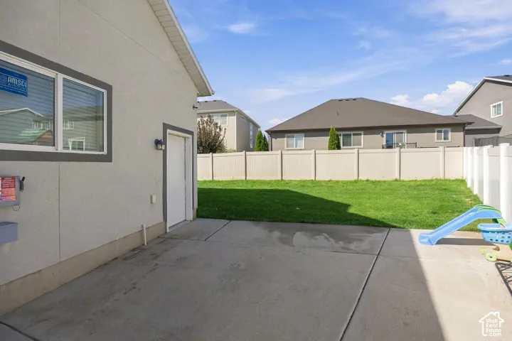 Expansive concrete patio with a stucco exterior, exterior lighting fixture, and a fully fenced yard featuring a manicured lawn