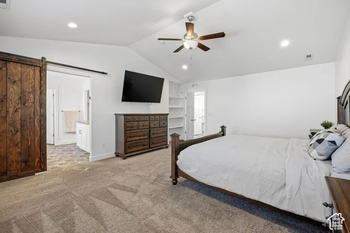Vaulted ceiling with a ceiling fan, recessed lighting, wood barn door, and built-in shelving