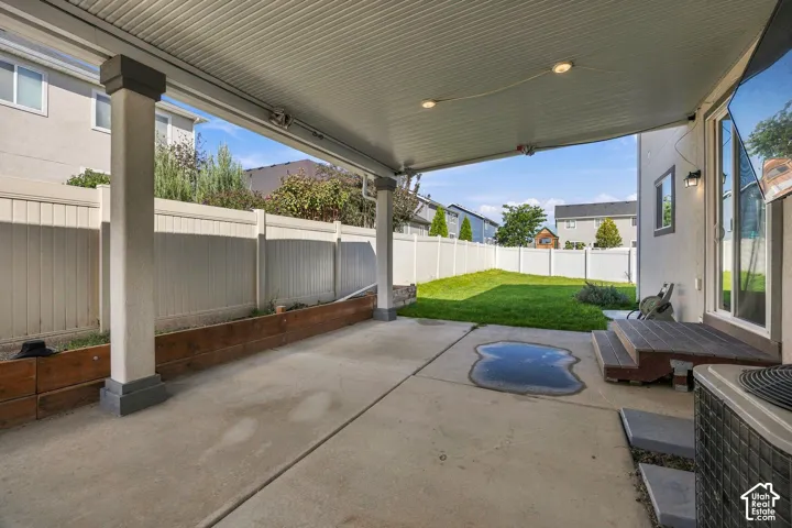 Covered concrete patio with recessed lighting and support columns, leading to a manicured lawn