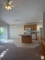 Vaulted ceiling with ceiling fan, tile flooring, wood cabinetry, built-in kitchen appliances, and sliding glass door