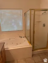 Soaking tub with integrated jets, glass-enclosed shower with gold-tone framing, and tiled flooring
