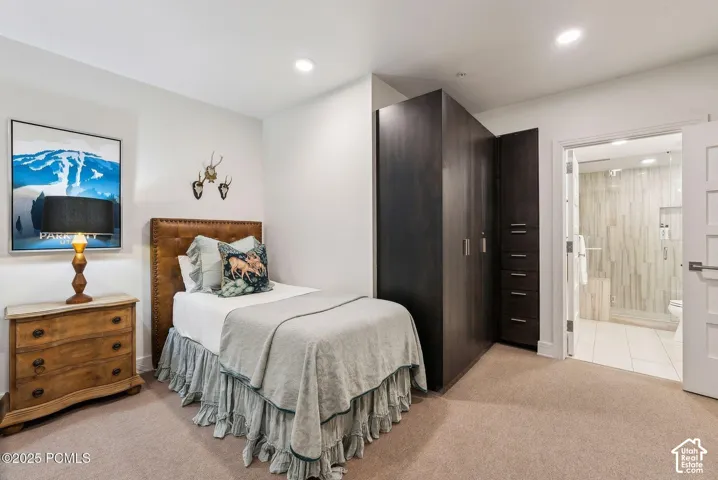 Recessed lighting, carpeting, built-in dark wood-finish wardrobe, and an ensuite bathroom featuring a glass-enclosed shower with vertical tile accents and a tiled floor