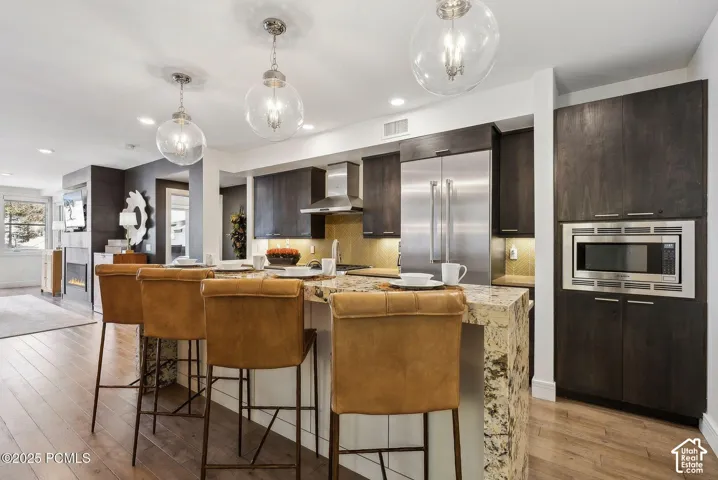 Kitchen featuring wood-finish flooring, dark wood cabinetry, a built-in stainless steel microwave, and a stainless steel refrigerator