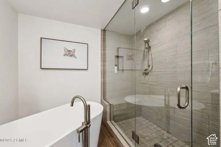 Freestanding soaking tub with a floor-mounted brushed nickel faucet, glass-enclosed shower with tile surround, built-in shower bench, and recessed lighting
