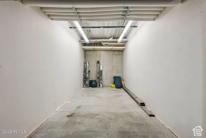 Concrete flooring with painted walls, exposed ceiling pipes, and fluorescent lighting
