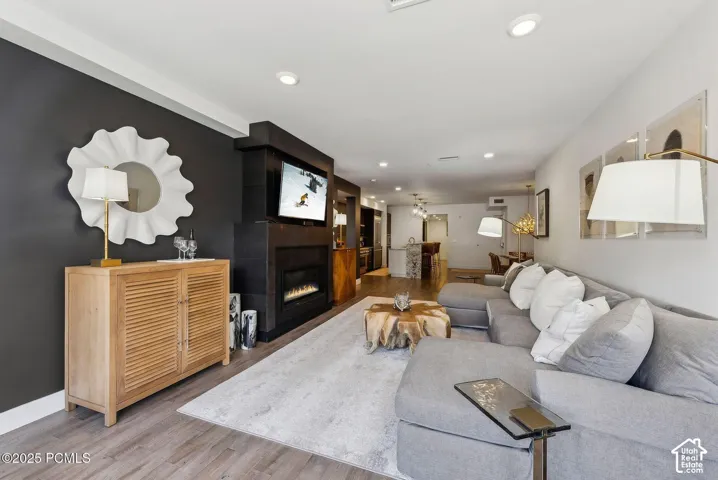 Open-concept living area featuring wood-finish flooring, a contemporary fireplace with a mounted television, recessed lighting, and a dark accent wall