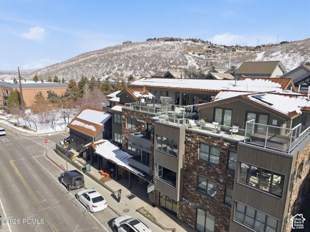 Multi-story building featuring stone and wood-finish siding, multiple private balconies with glass railings, and a prominent rooftop terrace