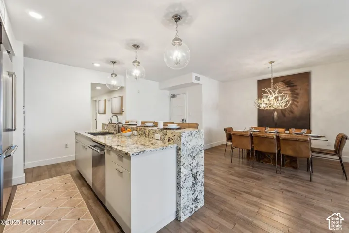 Open-concept living space with wood-finish flooring, a kitchen island featuring a stone countertop and waterfall edge, stainless steel appliances, and spherical pendant lighting