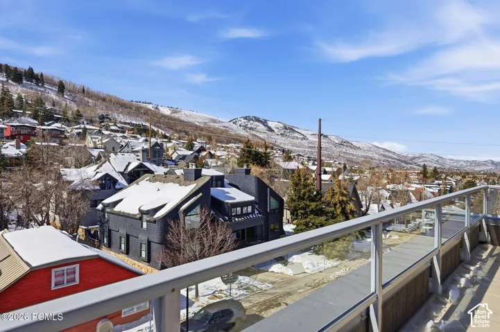 Expansive outdoor balcony with glass railing, showcasing a sloped mountain backdrop and a residential neighborhood